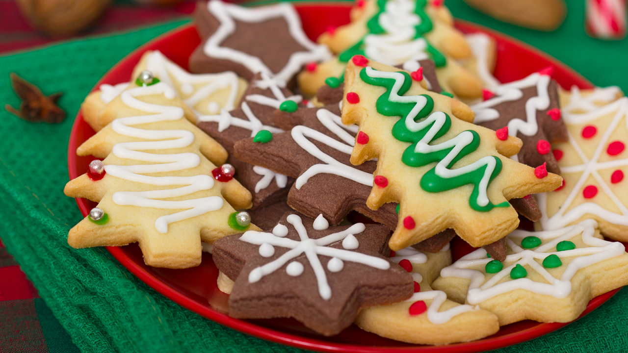 Red plate full of decorated Christmas cookies on a green table cloth.